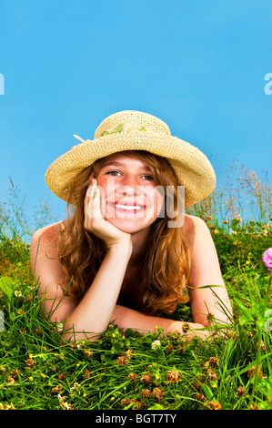 Junge Teenager-Mädchen Verlegung in Sommerwiese ruht Kinn auf Hand riechende Blume Stockfoto