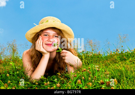 Junge Teenager-Mädchen Verlegung in Sommerwiese ruht Kinn auf Hand riechende Blume Stockfoto