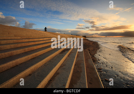 Ein Radfahrer fährt entlang des oberen Randes der Ufermauer an Heacham auf der Norfolk-Küste bei Sonnenuntergang. Stockfoto