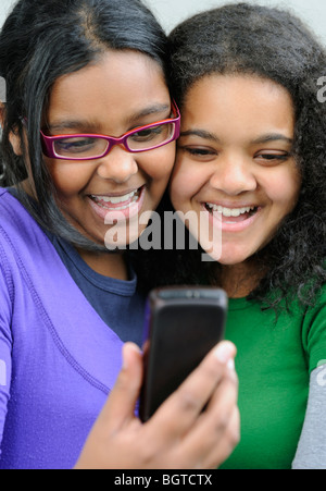 Mädchen im Teenageralter lachen während der Suche auf Handy, Cape Town, Western Cape, Südafrika Stockfoto