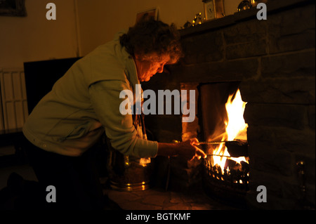 Die Rentnerin zündet ein offenes Feuer an, um sich in ihrem Haus warm zu halten, während sie versucht, die Strom- und Gasrechnungen in Großbritannien zu sparen Stockfoto