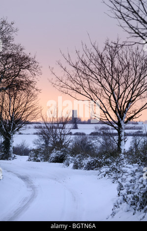 Winterlandschaft-Schnee-Szene der Feldweg mit Dorfkirche in Ferne, Norfolk, UK, Dezember Stockfoto