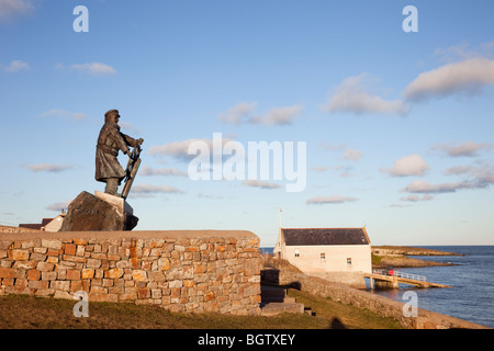 Statue von Coxswain Richard (DIC) Evans 1905-2001 mit der alten Rettungsboot Station dahinter. Moelfre, Anglesey, North Wales, Großbritannien Stockfoto