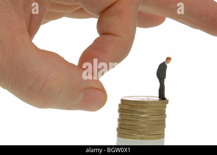 Menschenhand streichen eine Miniatur Geschäftsmann Figur aus einem Stapel von Münzen, symbolisches Bild für die Entlassung Stockfoto