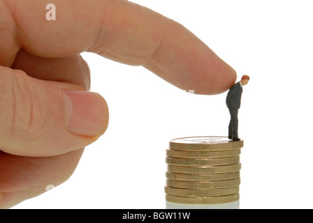 Menschenhand schob eine Miniatur Geschäftsmann Figur aus einem Stapel von Münzen, symbolisches Bild für die Entlassung Stockfoto