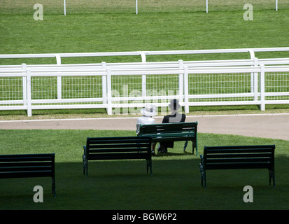 Ein paar elegant gekleidet, sitzen auf einer Bank im Royal Gehäuse in Royal Ascot Stockfoto