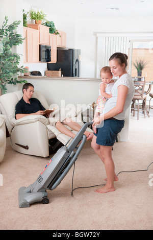 Eine Mutter versucht, Vakuum, während der Vater herum sitzt Stockfoto