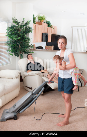 Eine Mutter versucht, Vakuum, während der Vater herum sitzt Stockfoto