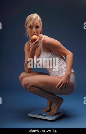 Junge Frau auf einer Skala und isst einen Apfel Stockfoto