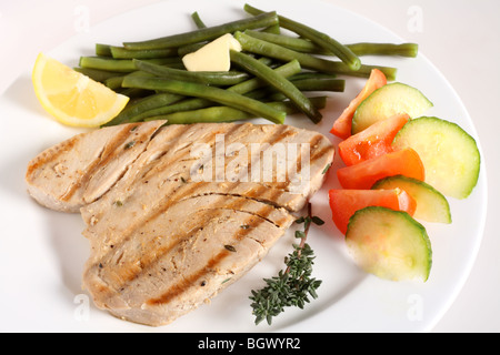 Eine Mahlzeit mit gegrilltem Thunfisch-Steak mit Salat aus Tomaten und Gurken und grüne Bohnen, mit einem Zweig Thymian und eine Zitronenscheibe Stockfoto