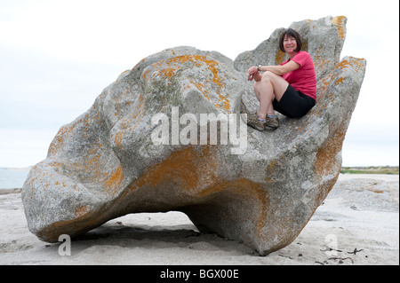 Eine 50 Jahre alte Frau sitzt auf einem großen Felsbrocken am Strand von Lesconil in der Nähe von Bénodet in der südlichen Bretagne, Frankreich Stockfoto