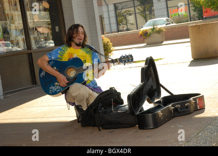 Das Foto zeigt ein Straßenkünstler Gitarre spielen und singen außerhalb auf einer öffentlichen Straße Ecke, Gitarrenkoffer offen für Beiträge. Stockfoto