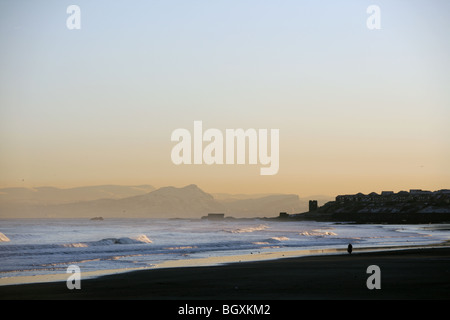 Eine einzelne Person zu Fuß am Strand entlang in Kirkcaldy mit Edinburgh im Hintergrund. Stockfoto