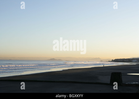 Eine einzelne Person zu Fuß am Strand entlang in Kirkcaldy mit Edinburgh im Hintergrund. Stockfoto