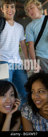 Zwei junge Freundinnen reden, während zwei junge Männer hinter ihnen stehen Stockfoto