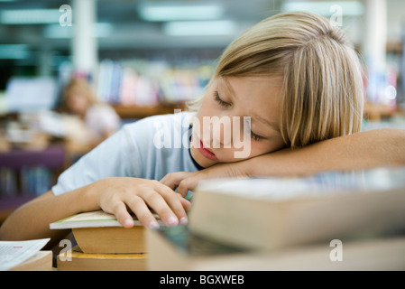 Junge Nickerchen mit Kopf ruht auf Arme in Bibliothek Stockfoto