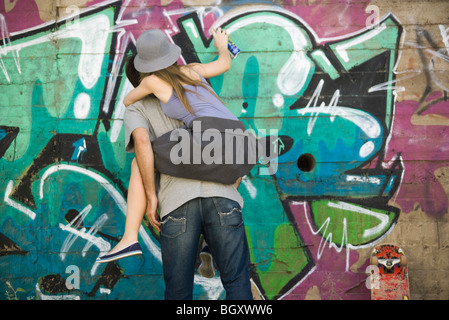 Junge Frau gebietsübergreifenden Gefährten zurück, sprühen Sie Malerei Graffiti Wandmalerei Stockfoto