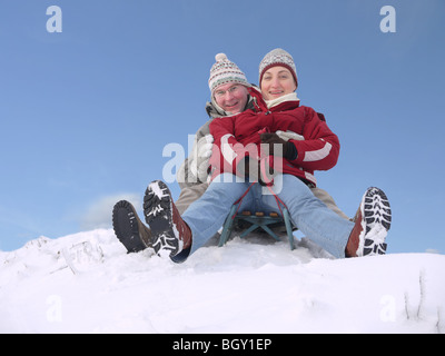 Junges Paar geht den Hügel hinunter auf Schlitten im winter Stockfoto