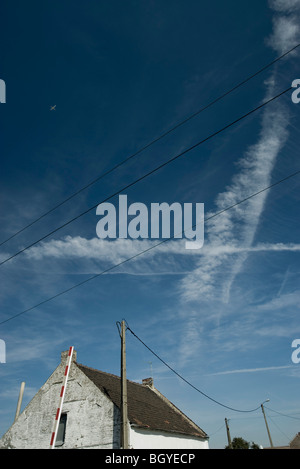 Vapor Trails und Flugzeug im blauen Himmel über Landhaus Stockfoto