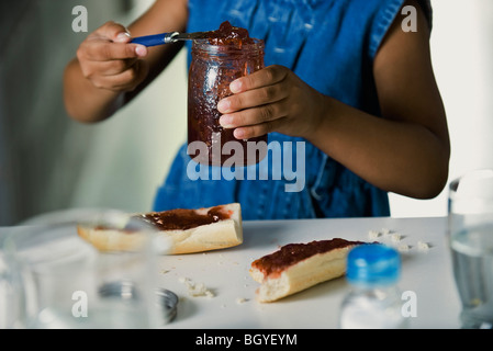 Mädchen Vorbereitung Snack von Brot und Marmelade, beschnitten Stockfoto