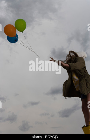 Weibchen beobachten als Bündel von Ballons schweben entfernt bis zu bewölktem Himmel Stockfoto