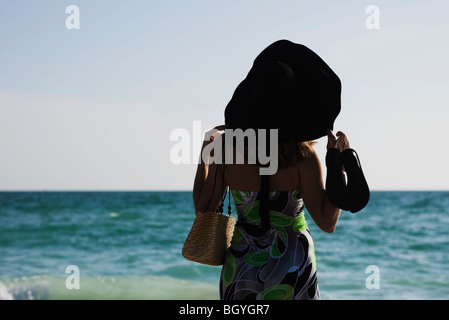 Frau trägt Sommerkleid und großen Sonnenhut, am Strand, Blick auf See Stockfoto