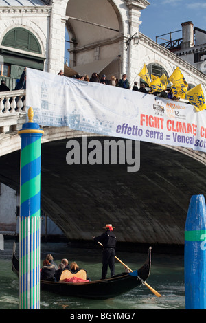 Demonstranten mit gelben Fahnen gegen globale Erwärmung über die Rialto-Brücke und Gondel mit Touristen sammeln Stockfoto