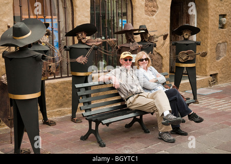 Amerikanischer Tourist paar auf Bank mit Metall-Skulptur-Mariachi-Band in Tlaquepaque, Guadalajara, Mexiko. Stockfoto