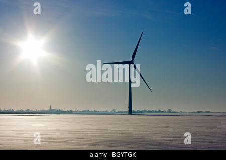 Windkraftanlage im Schnee, gegen blauen Winterhimmel mit der aufgehenden Sonne, dominiert von einer flachen Fenland-Landschaft Stockfoto