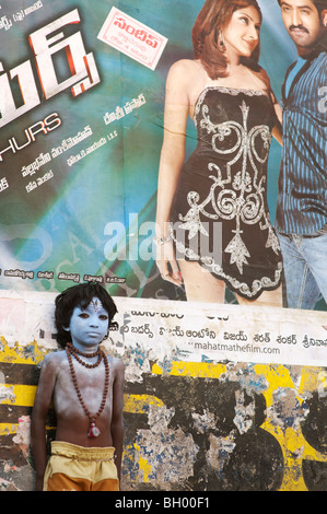 Indischer Junge, Gesicht gemalt als Hindu Gott Shiva vor einem Bollywood Film Poster. Andhra Pradesh, Indien Stockfoto