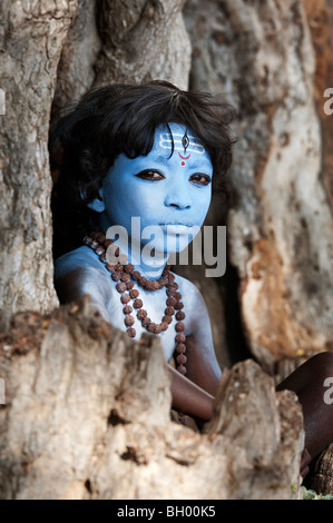 Indischer Junge, Gesicht gemalt als Hindu Gott Shiva in einem alten Baumstumpf sitzen. Andhra Pradesh, Indien Stockfoto