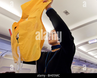 Ein asiatisch-amerikanische Flugbegleiter veranschaulicht richtig Leben Weste Verwendung für abfliegende Passagiere. Stockfoto