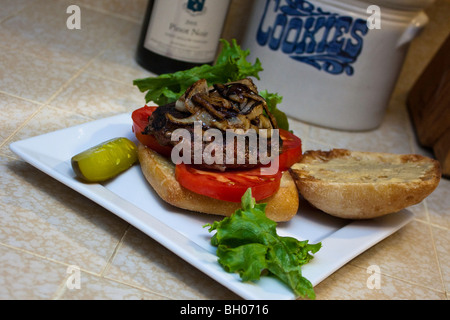 Ein Ciabatta-Burger mit Salat, Tomaten und gegrillte Zwiebel mit eine Gurke auf der Seite Stockfoto