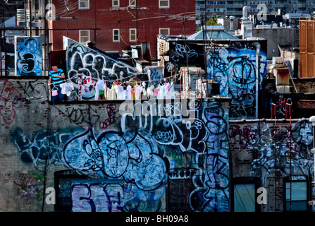 Ein asiatischer Mann hängt seine Familie Wäsche zum Trocknen auf einem Graffiti-bedeckten Dach in Chinatown, Lower Manhattan, New York City. Stockfoto