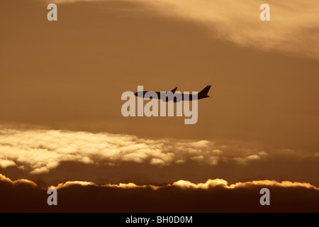 Flugreisen. Passagierflugzeug fliegt bei Sonnenuntergang in der Luft gegen einen bewölkten Himmel. Silhouette des Flugzeugs in Flugbahn. Zivilluftfahrt. Stockfoto