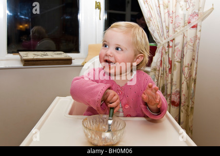 Horizontal nahe Porträt eines Mädchens in einem Durcheinander in ihrem Hochstuhl Schokoladeneis zu essen bekommen. Stockfoto