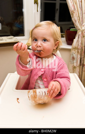 Vertikale nahe Porträt eines Mädchens in einem Durcheinander in ihrem Hochstuhl Schokoladeneis zu essen bekommen. Stockfoto