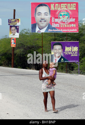 Eine Frau und Kind Fuß auf der Straße vorbei an politischen Plakatwerbung, Südwest Dominikanische Republik Stockfoto