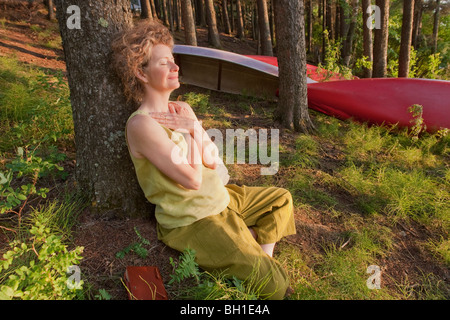 Frau lehnt sich gegen Baum mit Hände gefaltet über Brust, Clear Lake, Manitoba Stockfoto