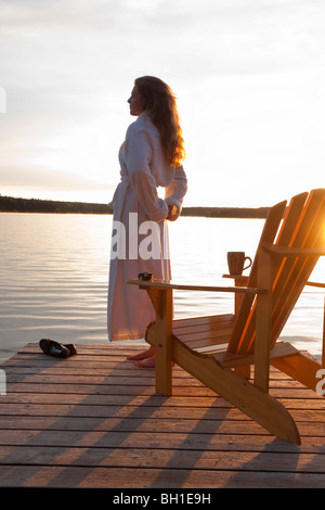 Frau im Bademantel stehen auf dock bei Sonnenaufgang, Clear Lake, Manitoba, Kanada Stockfoto