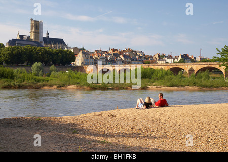 Junges Paar sitzt an den Ufern des Flusses Loire, Saint Cyr et Sainte-Julitte-Kathedrale im Hintergrund Brücke über th Stockfoto