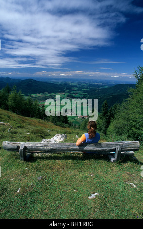 Junge Frau sitzt auf der Bank in der Nähe von Almhütte Kohleralm, Blick auf Inzell, Kohler-Alm, Chiemgau Palette, Chiemgau, Bayerische Voralpen Stockfoto