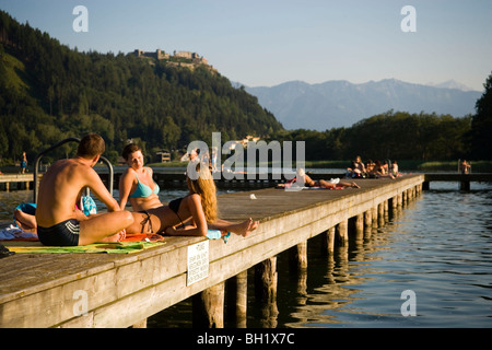 Junge Leute, Sonnenbaden am Boardwalk, Burg Landskron im Hintergrund, Ossiacher See, Ossiach, Kärnten, Österreich Stockfoto
