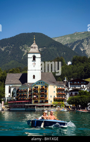 Blick über See Wolfgangsee, Pfarr-und Wallfahrtskirche und Hotel Im Weissen Roessel bin Wolfgangsee, Menschen in eine elektrische Bo Stockfoto