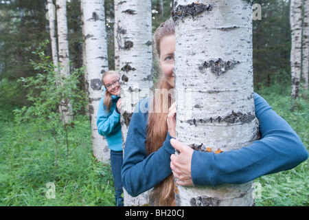 Frau und Mädchen herausschauen hinter Bäumen im Hain, Manitoba, Kanada Stockfoto