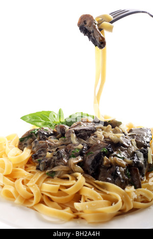 Eine Mahlzeit mit Fettuccini mit Pilzen, Zwiebeln und Knoblauch in einer Creme-Petersilie-Sauce, serviert mit einem Zweig Basilikum. Stockfoto