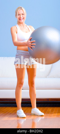 Junge Frau trägt Sportswear hält einen Balance-Ball in einem Wohnzimmer. Vertikale erschossen. Stockfoto