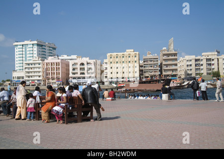 Dubai Vereinigte Arabische Emirate Gruppe der indischen Touristen sitzen draussen in der Sonne auf hölzernen Bänken mit Blick über den Dubai Creek. Stockfoto