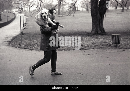 Der Beste Freund Des Mannes. Ein Mann, der mit dem Hund Hyde Park London spaziert und einen alten Hund über seine Schultern trägt. 1979 1970S GB HOMER SYKES Stockfoto