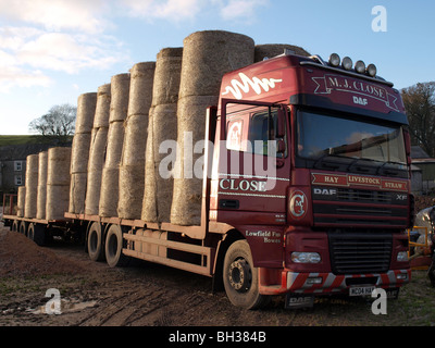 Heu-LKW mit Fahrertür öffnen und Anhänger beladen mit drei Reihen von runden Ballen in einem schlammigen Hof an sonnigen Wintertag Stockfoto